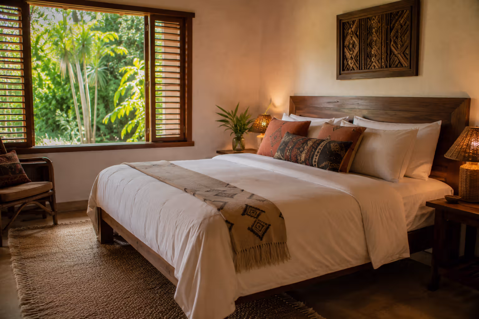 Neatly made cottage bedroom with white linen, ethnic cushions and garden window view