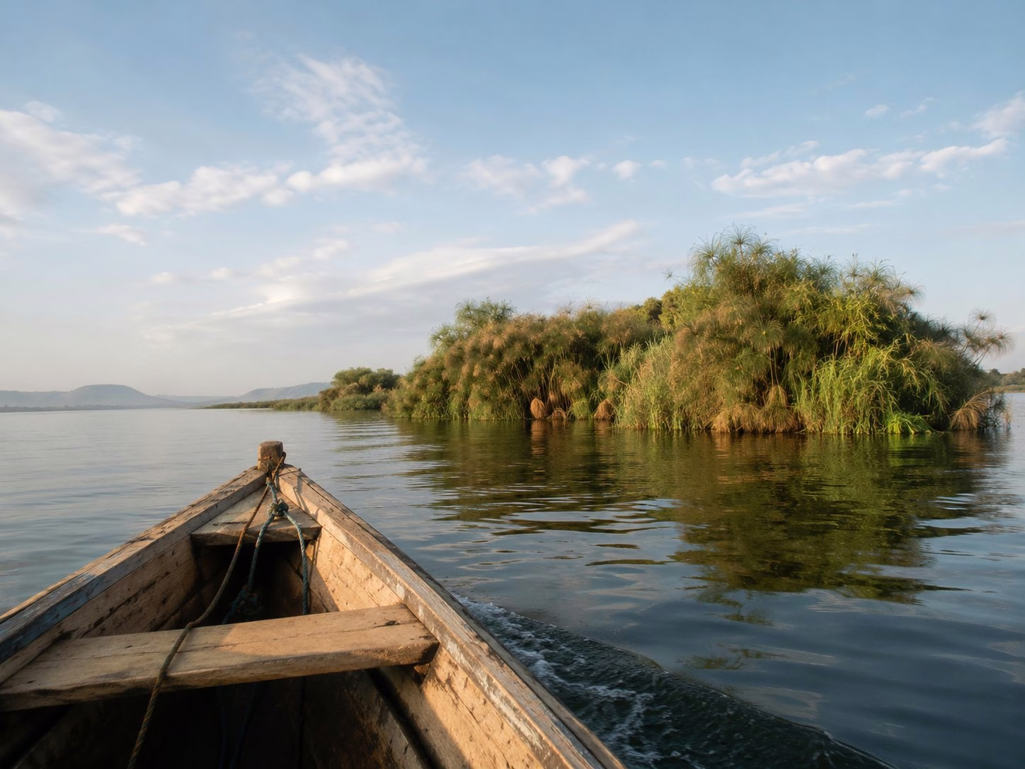 Wooden boat approaching papyrus islands on Lake Victoria, calm water and blue sky